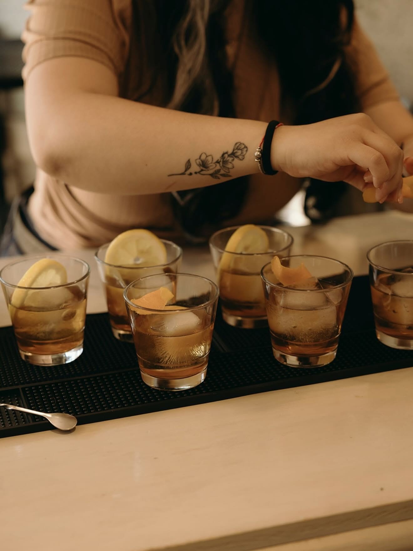 Detail shot of a Sips & Shots bartender garnishing a lineup of old fashioneds
