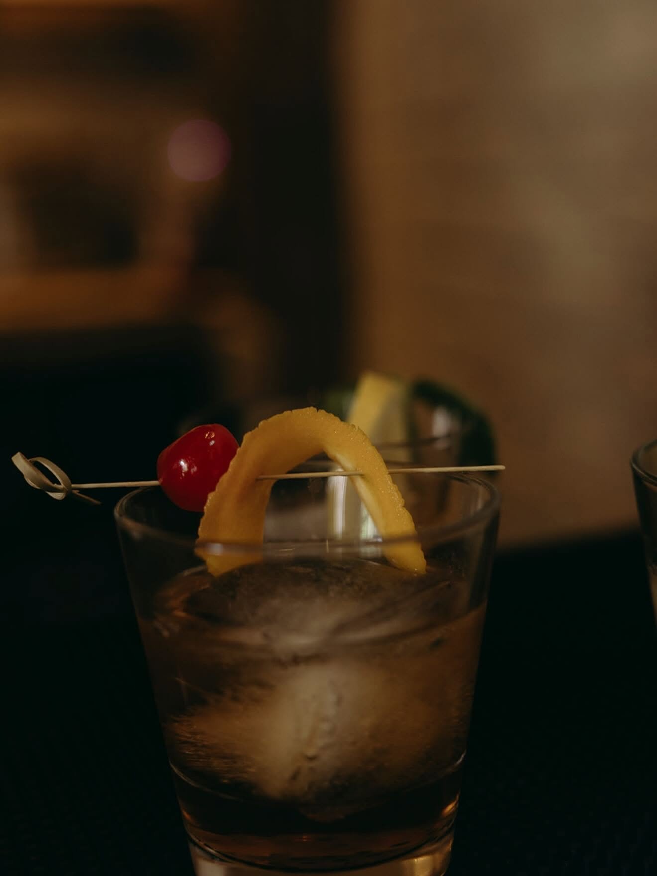 Close-up of an old fashioned garnished with cherry and orange peel